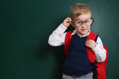 Photo of Cute little child wearing glasses near chalkboard, space for text. First time at school