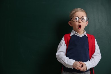 Photo of Cute little child wearing glasses near chalkboard, space for text. First time at school