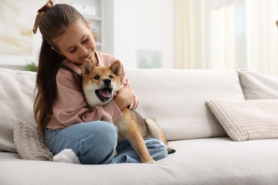 Photo of Cute little girl hugging her dog on sofa at home, space for text. Child and pet