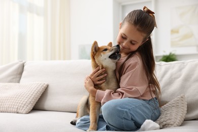 Photo of Cute little girl hugging her dog on sofa at home, space for text. Child and pet