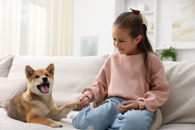 Photo of Cute little girl with her dog on sofa at home. Child and pet