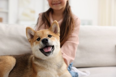 Photo of Cute dog and smiling little girl on sofa at home, closeup