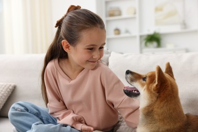 Photo of Cute little girl with her dog on sofa at home. Child and pet