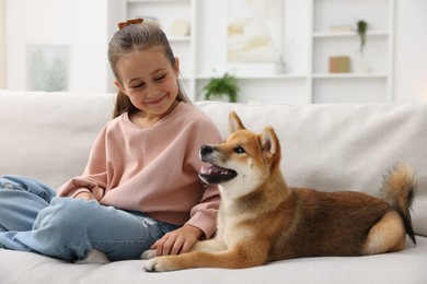 Photo of Cute little girl with her dog on sofa at home. Child and pet