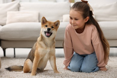Photo of Cute little girl with her dog on floor at home. Child and pet