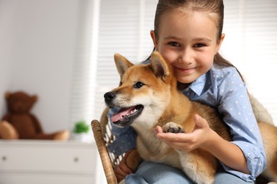 Photo of Portrait of cute little girl with her dog on chair at home, space for text. Child and pet