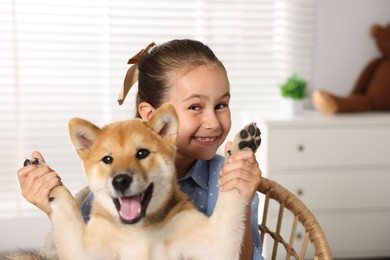 Photo of Portrait of smiling little girl with her dog on chair at home. Child and pet