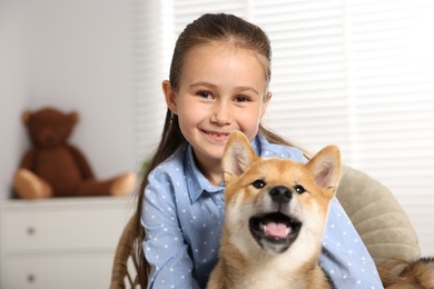 Photo of Portrait of smiling little girl with her dog on chair at home. Child and pet