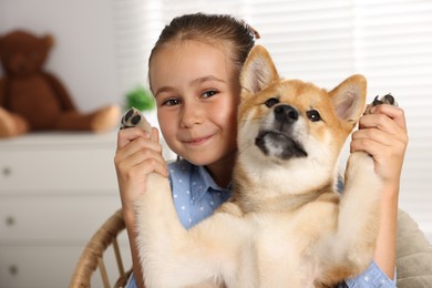 Photo of Portrait of cute little girl with her dog on chair at home. Child and pet