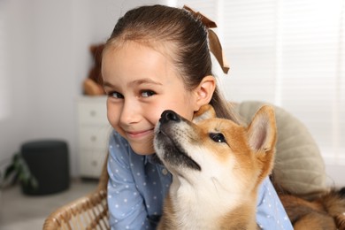 Photo of Portrait of cute little girl with her dog on chair at home. Child and pet