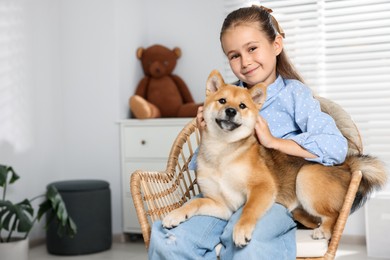 Photo of Portrait of cute little girl with her dog on chair at home, space for text. Child and pet