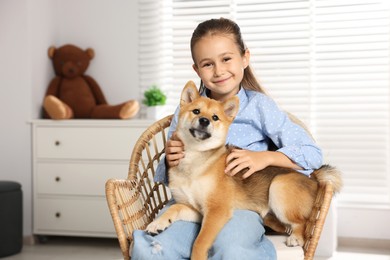 Photo of Portrait of cute little girl with her dog on chair at home. Child and pet
