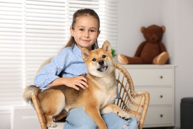 Photo of Portrait of cute little girl with her dog on chair at home. Child and pet
