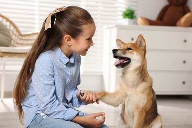 Photo of Cute little girl with her dog on floor at home. Child and pet
