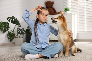 Photo of Cute little girl feeding her dog on floor at home. Child and pet