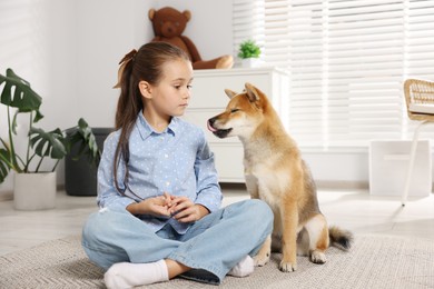 Photo of Cute little girl with her dog on floor at home. Child and pet
