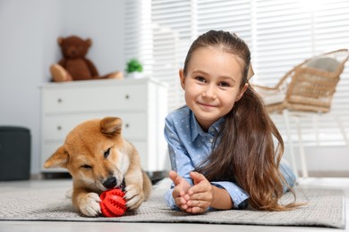 Photo of Portrait of cute little girl with her dog and pet toy on floor at home