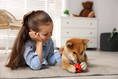 Photo of Cute little girl with her dog and pet toy on floor at home