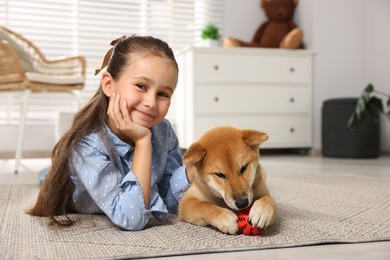 Photo of Portrait of cute little girl with her dog and pet toy on floor at home