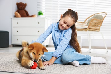 Photo of Smiling little girl with her dog and pet toy on floor at home