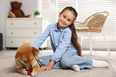 Photo of Cute little girl with her dog and pet toy on floor at home