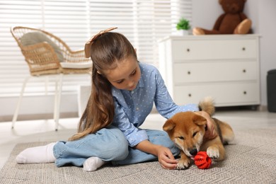 Photo of Cute little girl with her dog and pet toy on floor at home