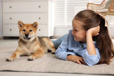 Photo of Cute little girl with her dog on floor at home. Child and pet