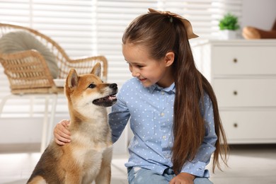 Photo of Smiling little girl with her dog on floor at home. Child and pet