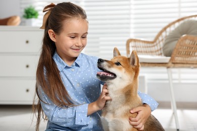 Photo of Cute little girl with her dog on floor at home. Child and pet