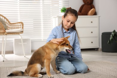 Photo of Cute little girl with her dog on floor at home. Child and pet