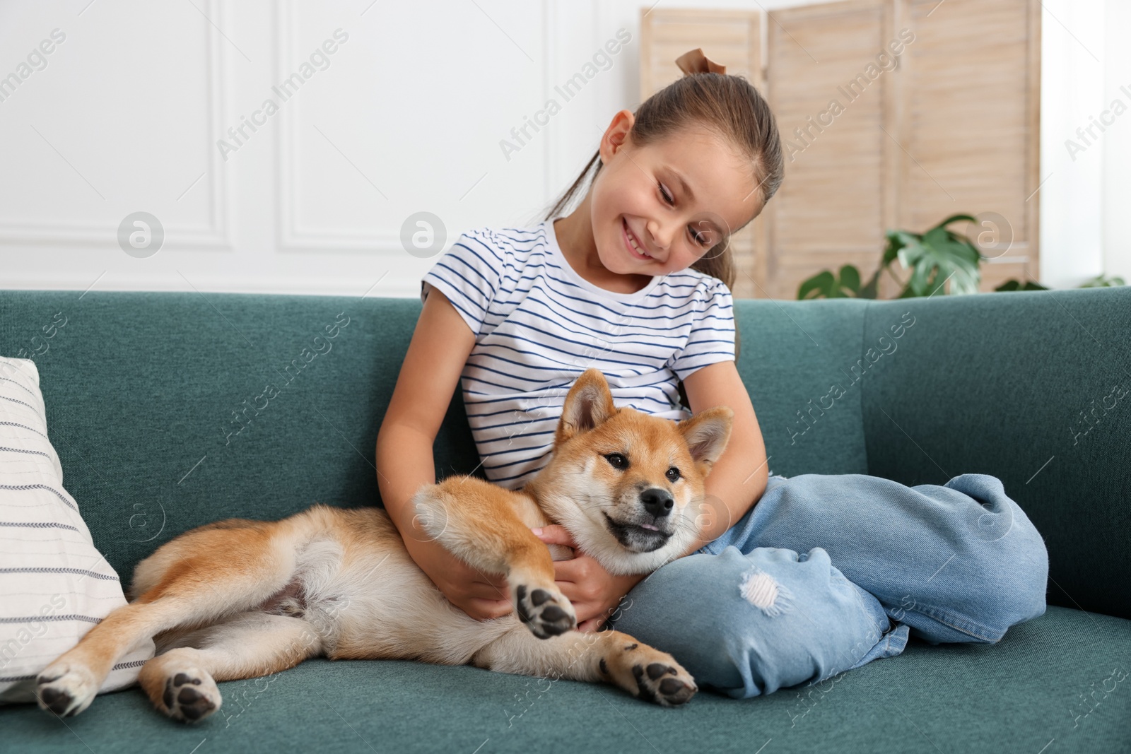 Smiling little girl with her dog on sofa at home. Child and pet Photo of Smiling little girl with her dog on sofa at home. Child and pet