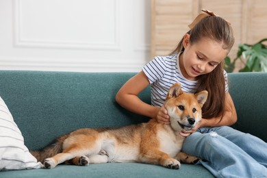 Photo of Cute little girl with her dog on sofa at home. Child and pet