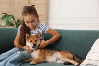 Photo of Cute little girl with her dog on sofa at home. Child and pet