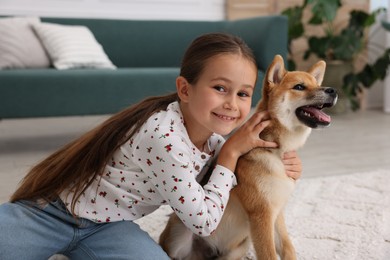 Photo of Portrait of smiling little girl with her dog on floor at home. Child and pet