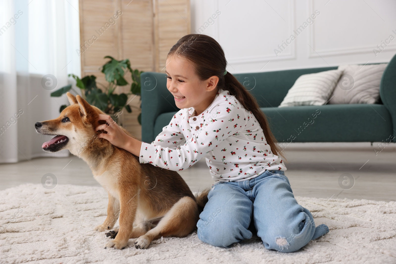 Photo of Smiling little girl with her dog on floor at home. Child and pet
