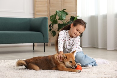 Photo of Cute little girl playing with her dog on floor at home. Child and pet