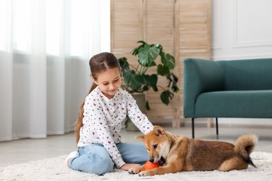Photo of Cute little girl playing with her dog on floor at home. Child and pet