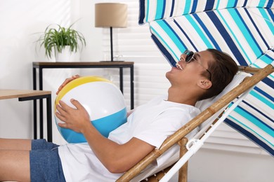 Photo of Happy man in sunglasses with beach ball having fun on sunbed at home. Dreaming about vacation at sea