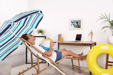 Photo of Happy man in sunglasses with beach ball having fun on sunbed at home. Dreaming about vacation at sea