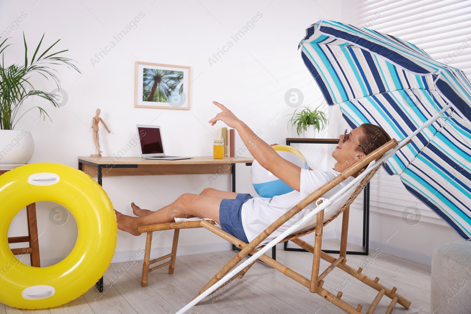 Photo of Happy man in sunglasses with beach ball having fun on sunbed at home. Dreaming about vacation at sea