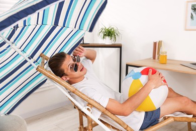 Photo of Happy man in sunglasses with beach ball having fun on sunbed at home. Dreaming about vacation at sea