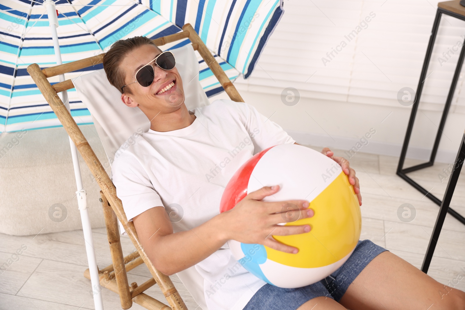 Happy man in sunglasses with beach ball having fun on sunbed at home. Dreaming about vacation at sea Photo of Happy man in sunglasses with beach ball having fun on sunbed at home. Dreaming about vacation at sea