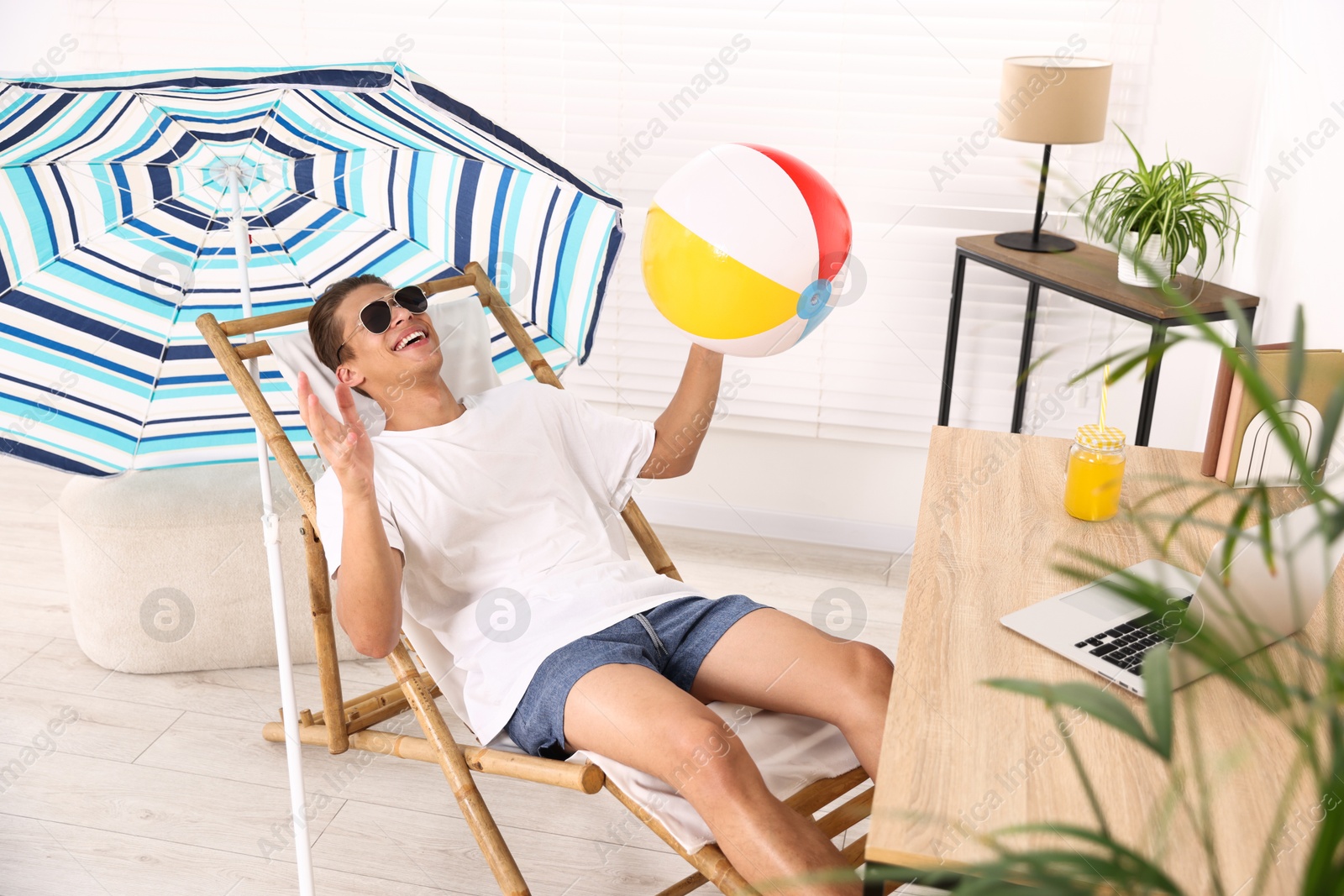 Happy man in sunglasses with beach ball having fun on sunbed at table indoors. Dreaming about vacation at sea Photo of Happy man in sunglasses with beach ball having fun on sunbed at table indoors. Dreaming about vacation at sea