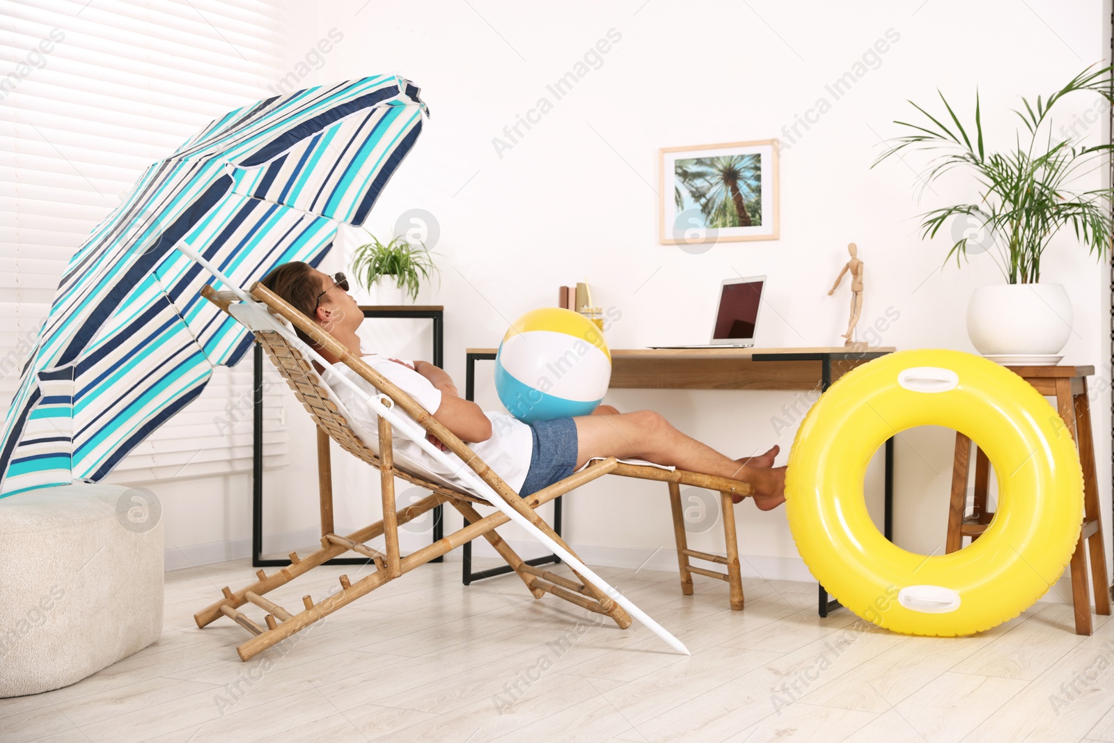 Man in sunglasses with beach ball having fun on sunbed at table indoors. Dreaming about vacation at sea Photo of Man in sunglasses with beach ball having fun on sunbed at table indoors. Dreaming about vacation at sea