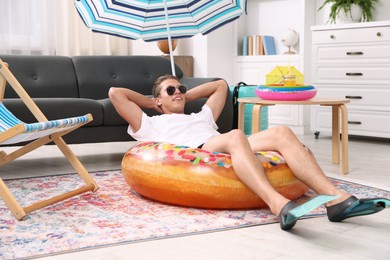 Photo of Happy man in sunglasses and flippers with inflatable ring having fun on floor at home. Dreaming about vacation at sea