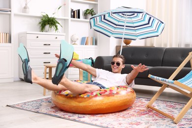 Photo of Happy man in sunglasses and flippers with inflatable ring having fun on floor at home. Dreaming about vacation at sea
