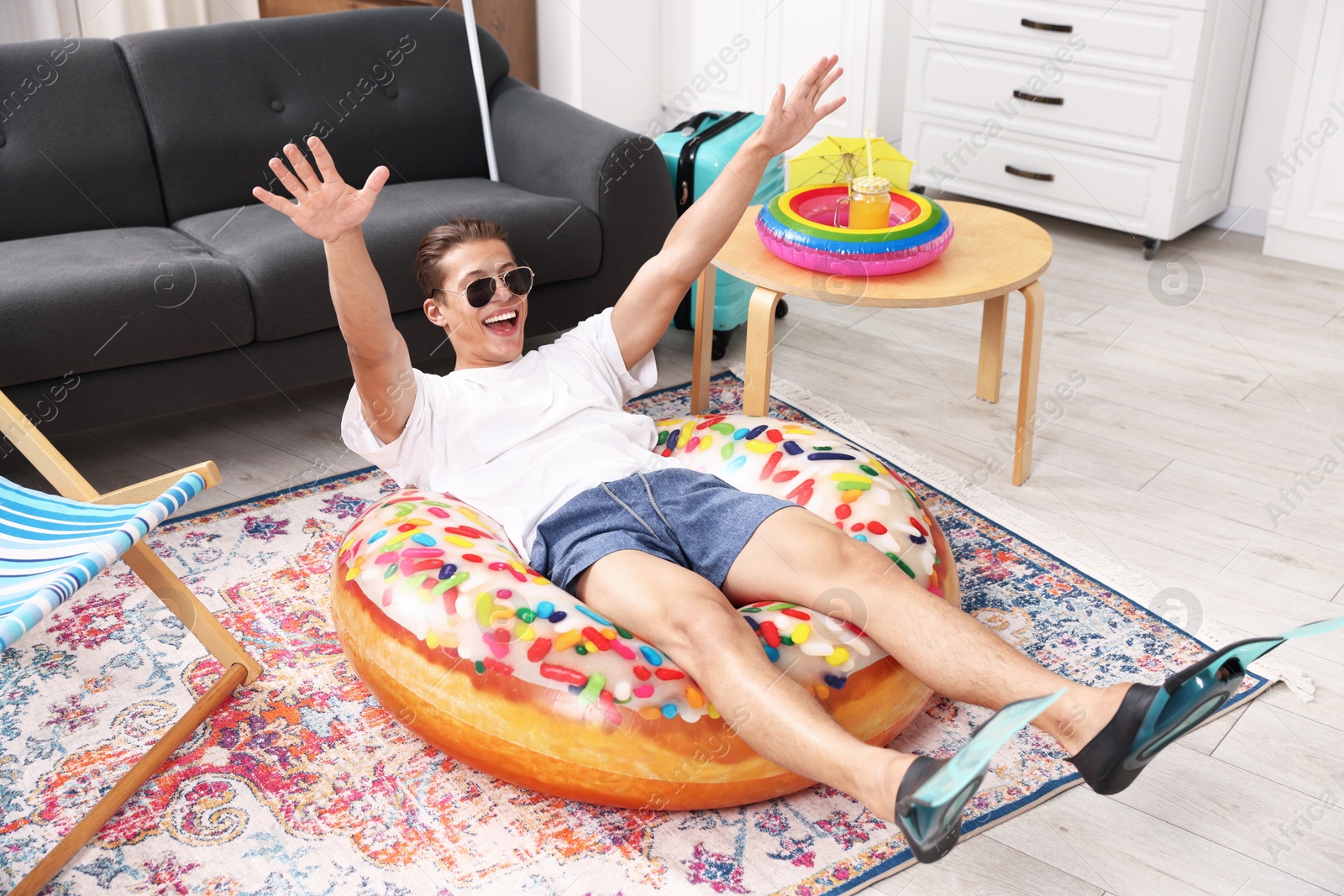 Happy man in sunglasses and flippers with inflatable ring having fun on floor at home. Dreaming about vacation at sea Photo of Happy man in sunglasses and flippers with inflatable ring having fun on floor at home. Dreaming about vacation at sea