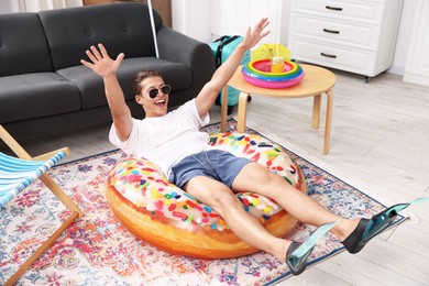 Photo of Happy man in sunglasses and flippers with inflatable ring having fun on floor at home. Dreaming about vacation at sea