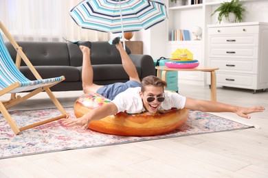 Photo of Happy man in sunglasses and flippers with inflatable ring having fun on floor at home. Dreaming about vacation at sea