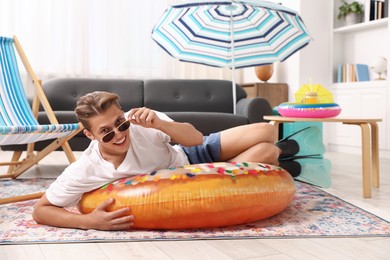 Photo of Happy man in sunglasses and flippers with inflatable ring having fun on floor at home. Dreaming about vacation at sea